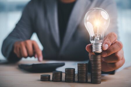 businessman hand holding lightbulb with coins stacking on desk.saving energy and money concept.の写真素材