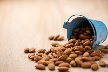 Almonds pour from blue bucket
 on wooden table. Almond concept with copyspace.の写真素材