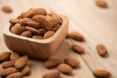 Almonds in wood bowl on light wood table. Almond concept with copyspace.の写真素材
