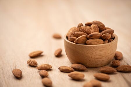 Almonds in wood bowl on light wood table. Almond concept with copyspace.の写真素材