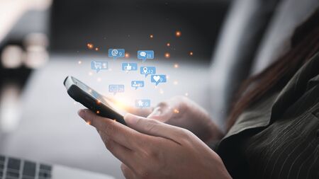 Social media interactions on mobile phone, concept with notification icons of like, message, email, comment and star above smartphone screen, person hands holding device, internet digital marketingの写真素材