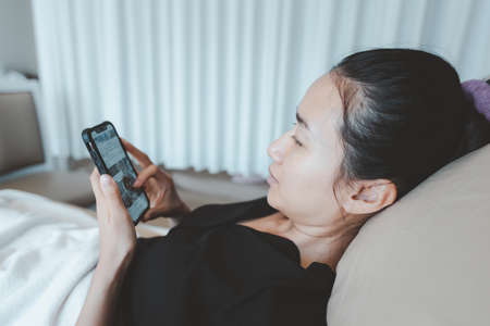 A beautiful woman lying on the hospital bed and Playing smartphone.