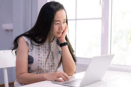 Beautiful asian girl using a notebook or laptop computer at her home and smiling happily.の写真素材