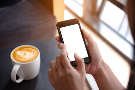 woman hand holding smartphone with blank screen in coffee shop for design or Advertisement.の写真素材