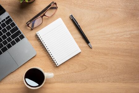 Wooden office desk table with blank notebook, laptop computer, cup of black coffee and supplies. Top view with copy space, flat lay.の写真素材