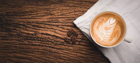 Coffee cup with latte art and beans on old wood table.there is space for ads,text,design and advertisement.の写真素材