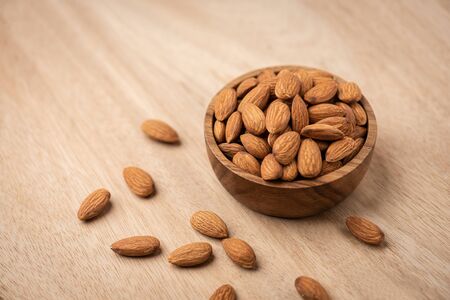Almonds in wood bowl on light wood table. Almond concept with copyspace.の写真素材
