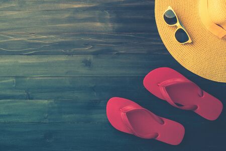 beach accessories on dark wood background. sunglasses, red flip-flops and yellow striped hat. summer is coming conceptの写真素材