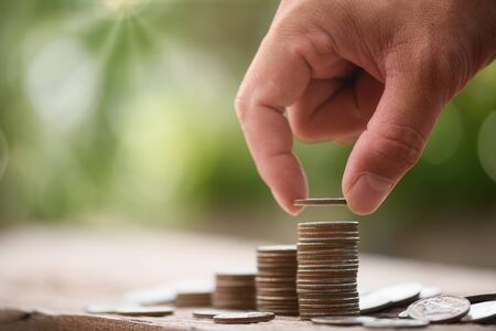 Hand putting coin on coin stack growing graph with green bokeh background,investment concept,Business Finance and Saving Money conceptの写真素材