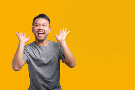 good looking Asian man is wearing a gray shirt Showing an excited expression with copy space on yellow summer background.の写真素材
