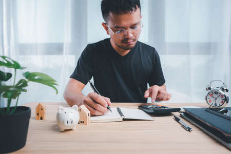 Businessman using calculators and notebooks to plan home payment installments.The concept of home installments, reducing principal and reducing interest.Asian man planning financial.の写真素材