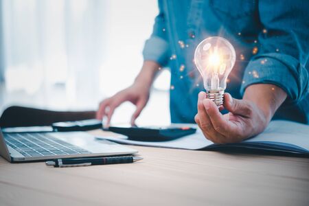 businessman hand holding lightbulb with office tools  on desk. idea, innovation inspiration concept.の写真素材