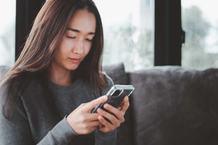 close up short beautiful asian woman using smartphone on the sofa relaxing corner in her house. she is stressed.の写真素材