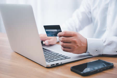 Hand holding credit card and using laptop. Businessman or entrepreneur working from home. Online shopping, e-commerce, internet banking, spending money, work from home concept.の写真素材