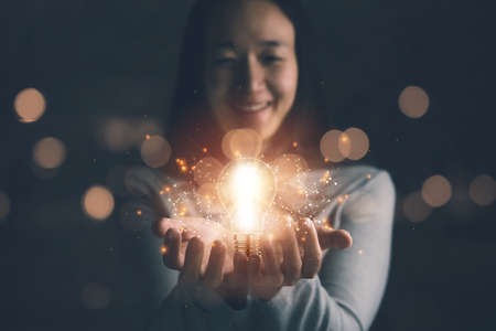 concept of creativity with bulbs that shine glitter.Hand of businesswoman holding illuminated light bulb, idea, innovation and inspiration concept.の写真素材