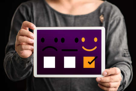 Customer evaluation feedback concept. Stylish men show him satisfaction on digital tablet with a checked box on smiley face rating.の写真素材