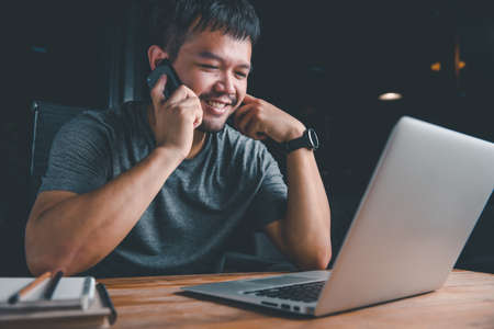 Photo of young asian good looking, successful and confident businessman. Young businessman working with computer and talking on phone.night time.concept work form home, stay at home.night time.の写真素材