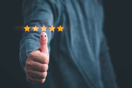 Customer satisfaction concept. Hand with thumb up Positive emotion smiley face icon and five star with copy space.の写真素材