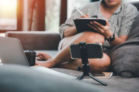 E learning concept,Business planning. Casual business woman writing on tablet and working Viewing online media from a smartphone on sofa at home. Woman studying online course and lecture on tablet.の写真素材
