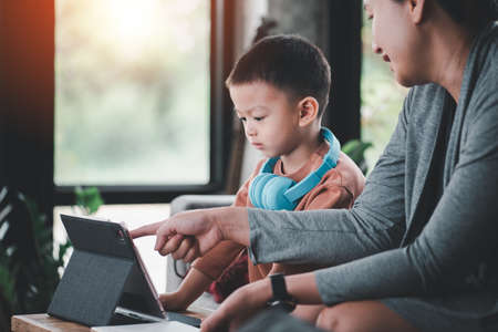 Cute Asian boy is learning from online technology using tablets. With a mother to teach and advise...
