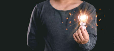 Idea innovation and inspiration concept.Hand of man holding illuminated light bulb, concept creativity with bulbs that shine glitter.Inspiration of ideas for sustainable business development.の写真素材