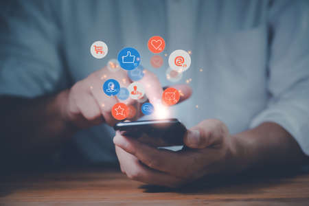 Social media interactions on mobile phone, concept with notification icons of like, message, email, comment and star above smartphone screen, person hands holding device, internet digital marketingの写真素材