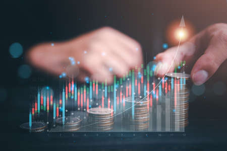 Finance and Investment concept.Money management and Financial chart. Businessman is showing a growing virtual hologram stock and rows of coins on dark tone background.の写真素材
