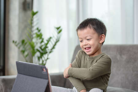 Asian boy with a cute face and good temper is looking and smiling at the camera in front of the tablet. While talking to friends via video call.の写真素材