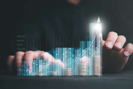 Finance and Investment concept.Money management and Financial chart. Businessman is showing a growing virtual hologram stock and rows of coins on dark tone background.の写真素材