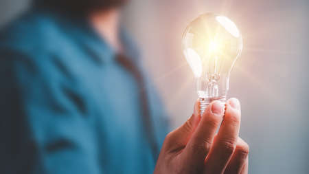 Idea innovation and inspiration concept.Hand of man holding illuminated light bulb, concept creativity with bulbs that shine glitter.Inspiration of ideas for sustainable business development.の写真素材