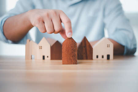 Real estate investment businessman hand choosing mini wood house model from model on wood table, Planning to buy property. concept of Choose the best.の写真素材