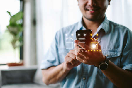 Customer service evaluation concept. Businessman pressing face smile emoticon show on virtual screen at smartphone.の写真素材