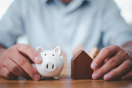 businessman holding a piggy bank and a house model for saving and investment ideas Stock Market Real Estate.の写真素材