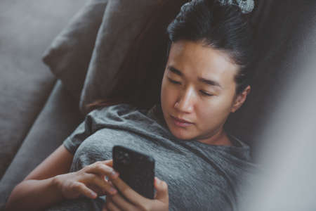 beautiful Asia women using smartphone on the sofa relaxing corner in her home.stay at home concept. Lifestyle with Technology concept.の写真素材