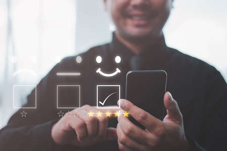 Customer service evaluation concept. Businessman pressing face smile emoticon show on virtual screen at smartphone.の写真素材