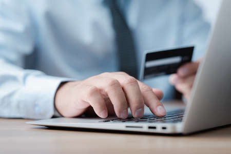 Close up of businessman hands holding a credit card and making a purchase using a laptop.の写真素材