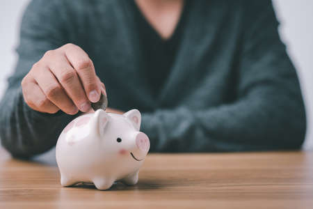 business finance saving and investment concept. hand put money coin into piggy bank for saving money wealth.の写真素材