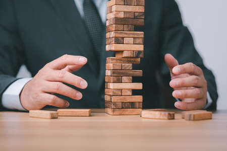 Planning, risk and strategy in business. Businessman holds the model of business, made from wood blocks. Alternative risk concept, business plan and business strategy. Insurance concept.の写真素材