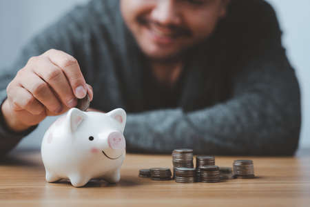 business finance saving and investment concept. hand put money coin into piggy bank for saving money wealth.の写真素材