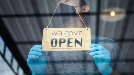 Owner retail shop wearing gloves and protective mask turning sign board to open store after close...