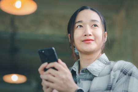 below view of cheerful Asian female office employee in stylish formal wear and holding mobile phone...
