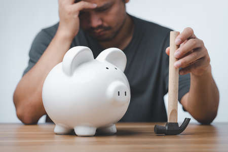 businessman was about to smash the piggy bank with a hammer to use the savings. a man smashes his piggy bank on a table.の写真素材