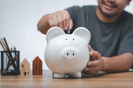business finance saving and investment concept. hand put money coin into piggy bank for saving money wealth.の写真素材