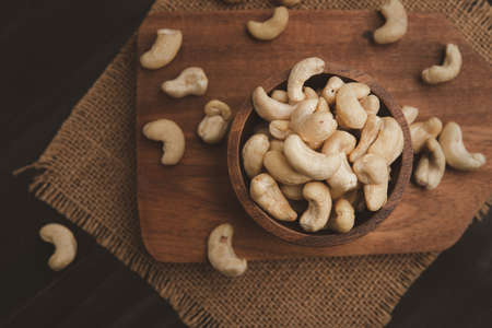 raw cashew nuts in wooden bowl on rustic table, healthy vegetarian snack