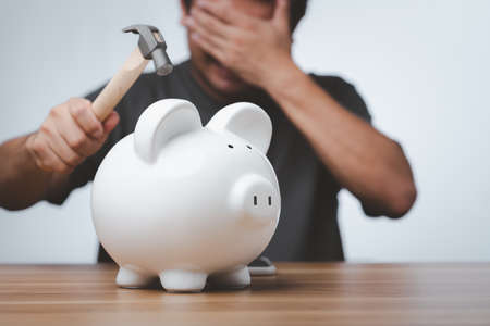 Male hand with hammer about to smash piggy bank to get at savings.の写真素材