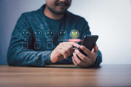 Customer service evaluation concept. Businessman pressing face smile emoticon show on virtual screen at smartphone.の写真素材
