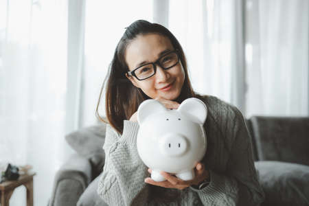 Happy smart asian woman saving money in a piggybank. saving and money concept.の写真素材