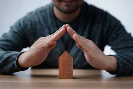 Property insurance and security concept. Protecting gesture of man and house model. Investment in real estate.の写真素材