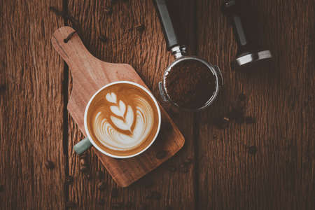 Latte art on hot latte coffee. Aroma coffee cup and coffee beans on wooden desk.の写真素材