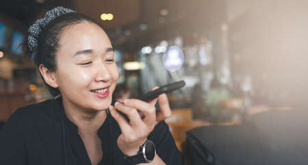 Young beautiful woman hold modern cellphone record voice message texting online, smart Asian female...